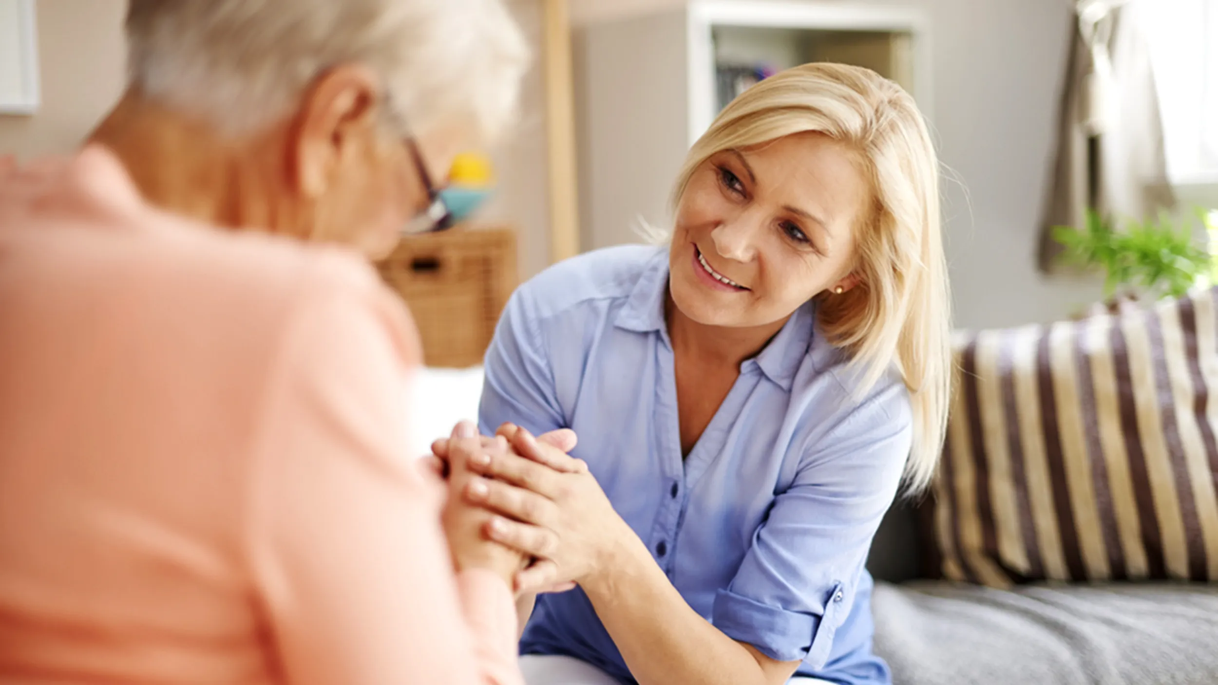 Grown daughter sitting hand in hand with elderly mother diagnosed with Alzheimer's 