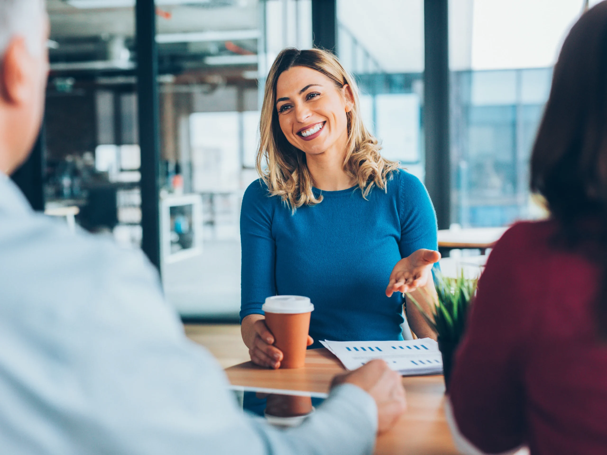 woman talking to couple with coffee in one hand